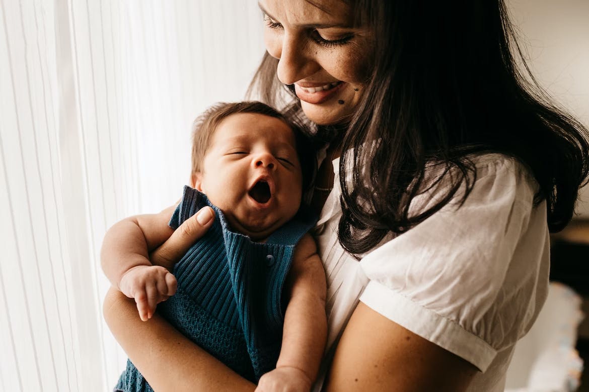 Baby yawning being held by a smiling woman