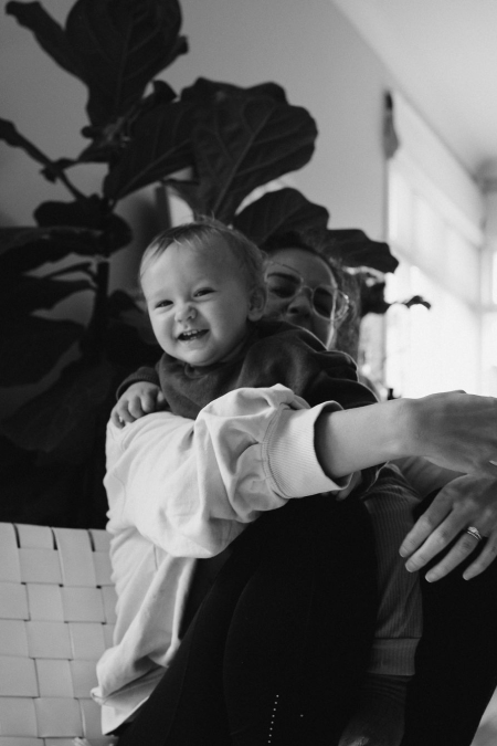 Woman holding baby boy smiling near pot plant