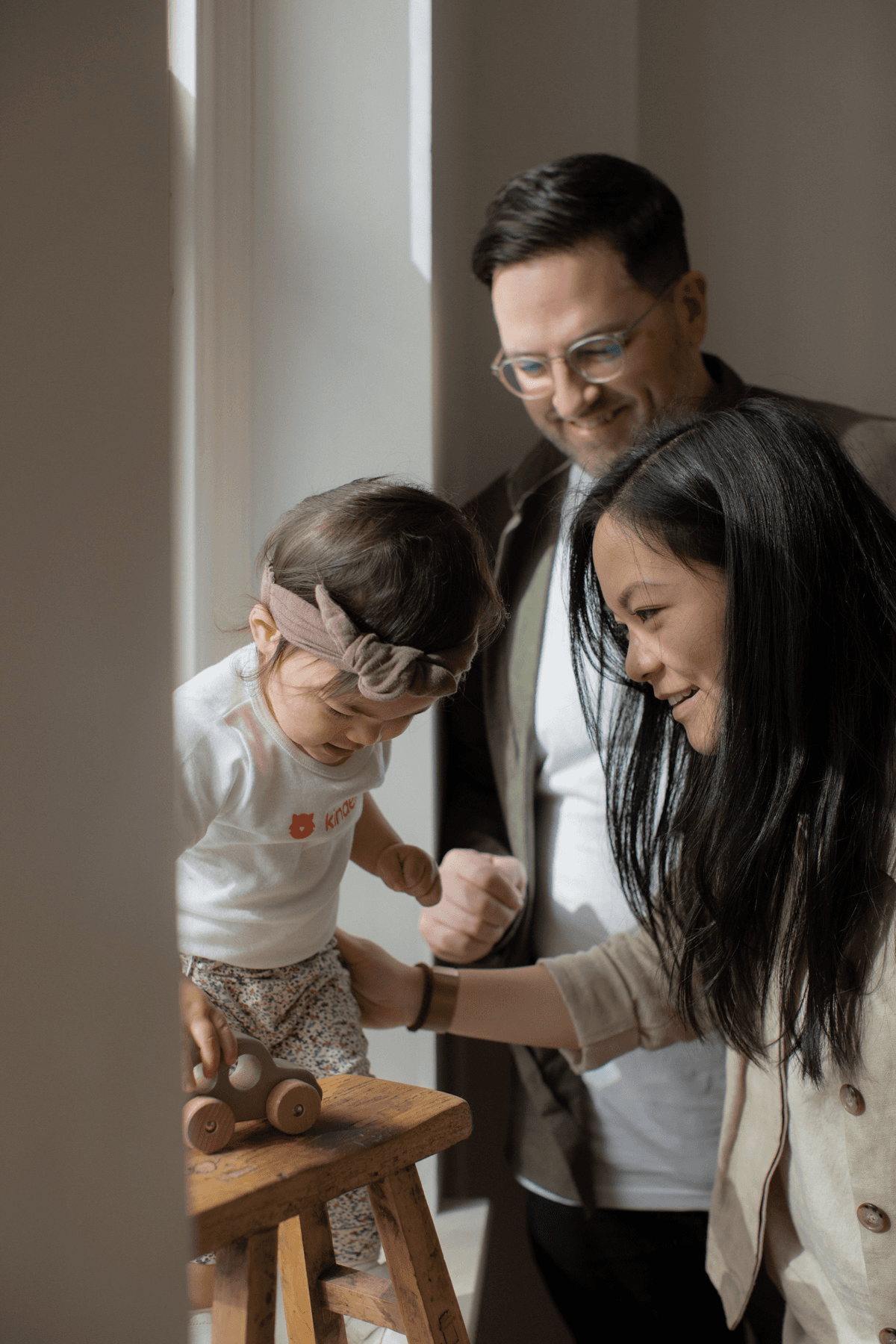 Mother and father with daughter in Kindello onesie play with wooden car
