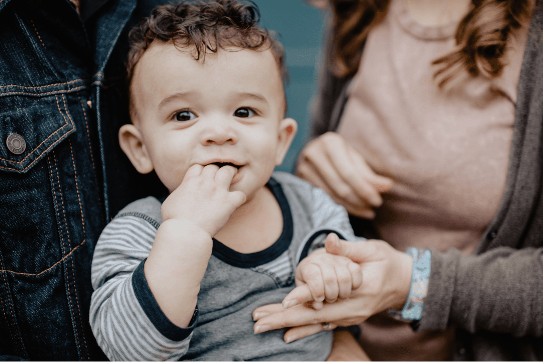 Young child smiling at the camera holding a woman's hand