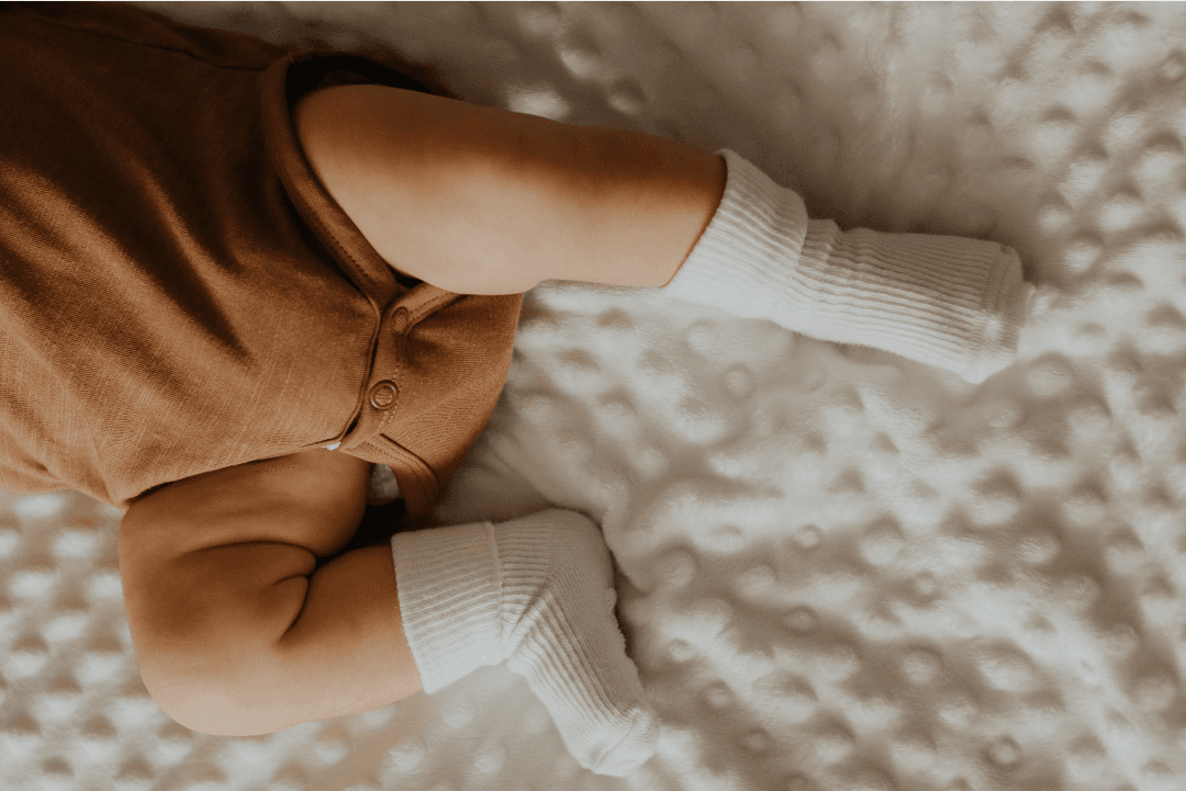 Close up of baby lying on mattress with brown pants and white socks on