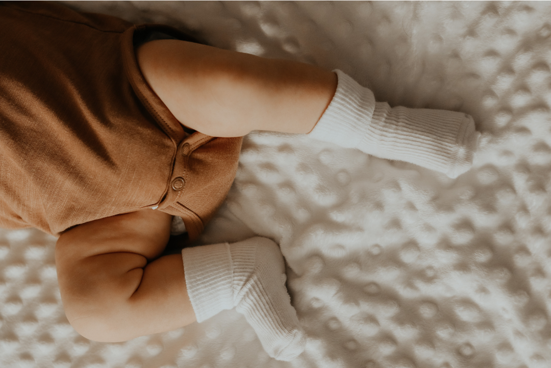 Close up of baby lying on mattress with brown pants and white socks on
